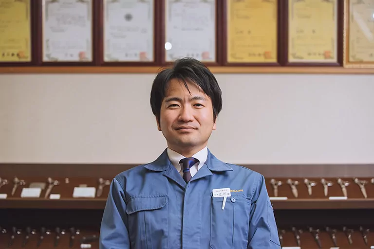Koshi Yamamura stands in front of rows of scissors and sushi knives